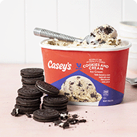 container of cookies and cream ice cream with a scoop sticking out the top, with a pile of oreos next to the container.